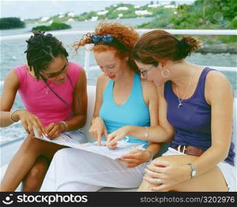 Close-up of three young women sitting on a bench and looking at a map, Bermuda