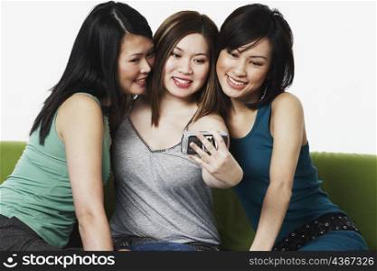 Close-up of three young women taking a photograph of themselves with a mobile phone camera