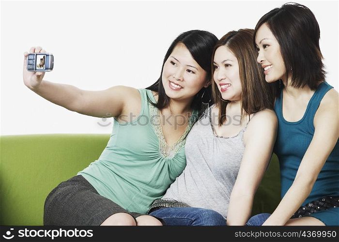 Close-up of three young women taking a photograph of themselves with a mobile phone camera