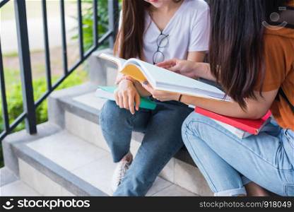 Close up of two Asian beauty girls reading and tutoring books for final examination together. Student smiling and sitting on stair. Education and Back to school concept. Lifestyles and People theme.