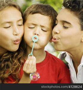 Close-up of two boys and a girl blowing bubble with a bubble wand