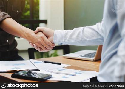 Close-up of two business executives shaking hands with data documents on the table