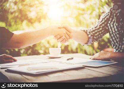 Close-up of two business people shaking hands while sitting at the working place.. Close-up of two business people shaking hands while sitting at t