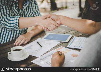 Close-up of two business people shaking hands while sitting at the working place.. Close-up of two business people shaking hands while sitting at t