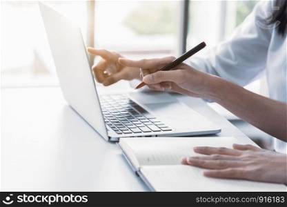 Close up of two businesswoman using laptop and writing on notebook in the morning. Business and financial concept. People and lifestyles concept. Office and workplace theme.