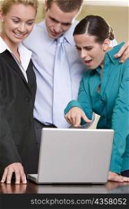 Close-up of two businesswomen and a businessman looking at a laptop