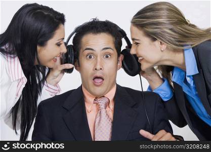 Close-up of two businesswomen pulling headphones of a businessman