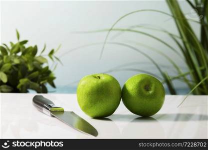 Close up of two delicious looking green apples next to a kitchen knife on a table on an out of focus background. Healthy and vegan food concept.. two delicious looking green apples next to a kitchen knife on a table. Healthy and vegan food concept.