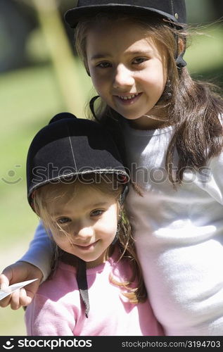 Close-up of two girls wearing riding hats and smiling