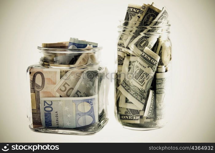 Close-up of two jars with Euros and dollar bills