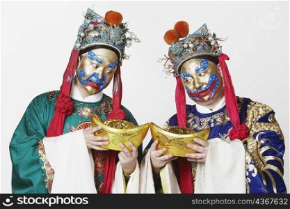 Close-up of two male Chinese opera performers looking at bowls full of gold coins