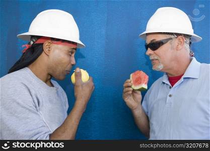 Close-up of two male construction workers face to face and eating fruits