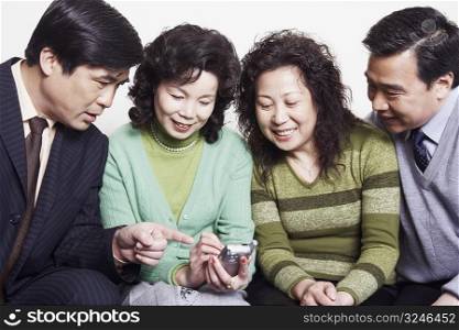 Close-up of two mature couples sitting together looking at a mobile phone