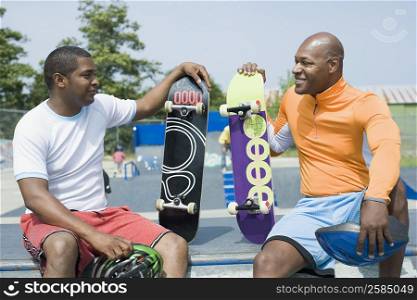 Close-up of two mature men sitting on skateboard ramp and smiling