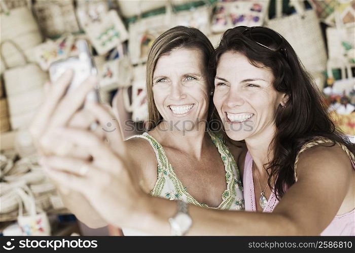 Close-up of two mid adult women holding a mobile phone and smiling