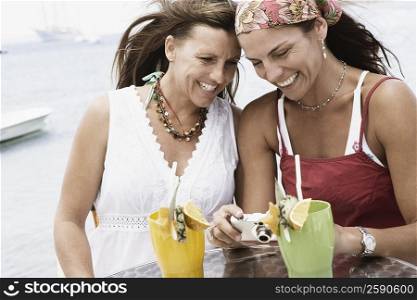 Close-up of two mid adult women looking at a digital camera and smiling