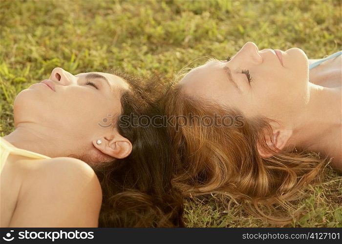 Close-up of two mid adult women lying on the grass with their eyes closed