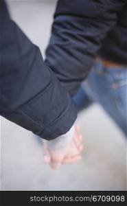 Close-up of two people holding hands and walking