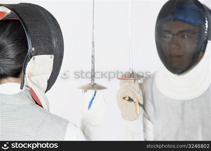 Close-up of two people wearing fencing masks and holding fencing foils