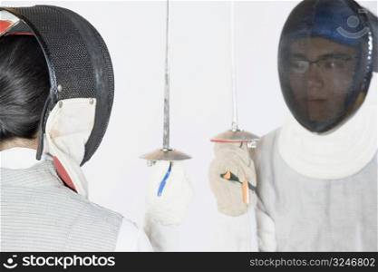 Close-up of two people wearing fencing masks and holding fencing foils