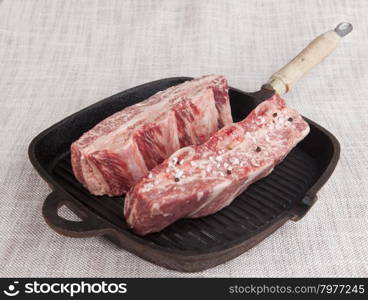 Close-up of two pieces of fresh marbled beef with sea salt and black pepper, on a cast-iron grill pan.