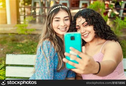 Close up of two smiling teenage girlfriends sitting on a bench taking a selfie, Two smiling teenage girlfriends taking a selfie sitting on a bench at sunset