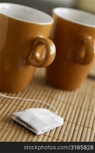 Close-up of two tea cups with a teabag on a bamboo mat