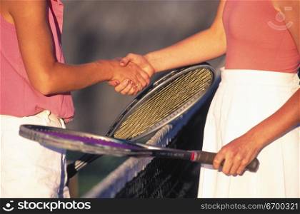 Close-up of two women shaking hands over a net on a tennis court