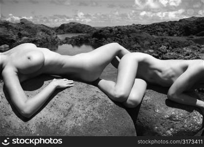 Close up of two young adult nude Caucasian women lying on boulders in Maui.
