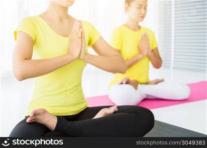 Close-up of Two young Asian women workout are hand of sitting in Lotus pose practicing yoga in yellow dress or pose with a trainer and practice meditation wellness lifestyle and health fitness concept