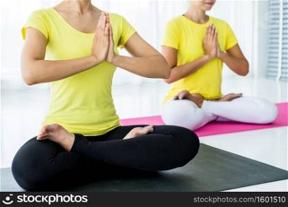 Close-up of Two young Asian women workout practicing yoga in yellow dress or pose with a trainer and practice meditation wellness lifestyle and health fitness concept in a gym.