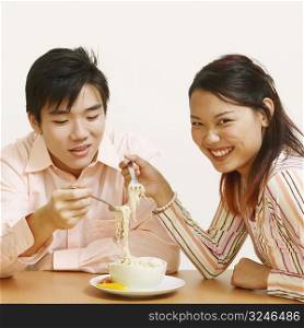 Close-up of two young couples eating noodles and smiling