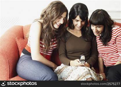 Close-up of two young women and a mid adult woman sitting on a couch and looking at a mobile phone
