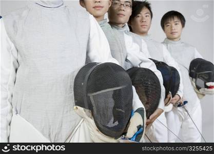 Close-up of two young women and three young men holding fencing masks with fencing foils