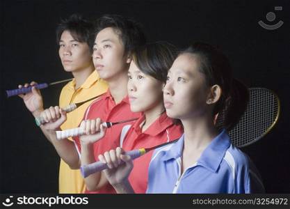Close-up of two young women and two young men standing side by side with badminton rackets