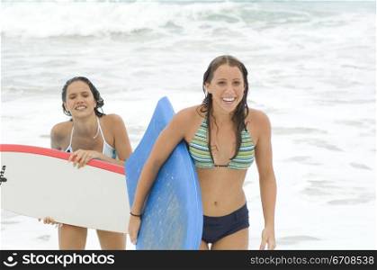 Close-up of two young women carrying surfboards