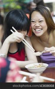 Close-up of two young women eating noodles with chopsticks