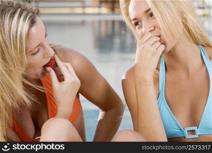 Close-up of two young women eating strawberries at the poolside