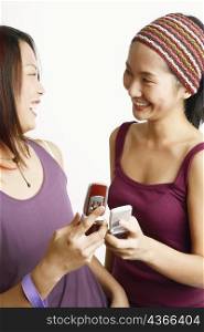 Close-up of two young women holding mobile phones and looking at each other
