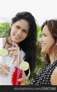 Close-up of two young women holding two glasses of cocktail and smiling
