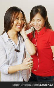 Close-up of two young women listening to music and smiling