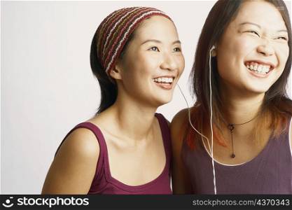 Close-up of two young women listening to music and smiling