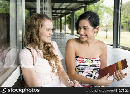 Close-up of two young women sitting in a corridor and smiling