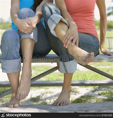 Close-up of two young women sitting on a picnic table in a park