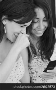 Close-up of two young women text messaging and smiling