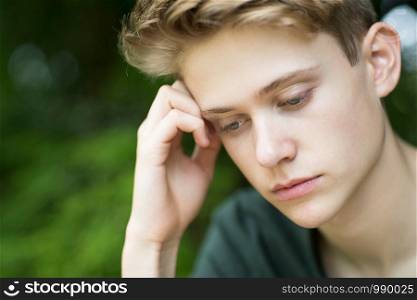 Close Up Of Unhappy Teenage Boy Sitting Outdoors