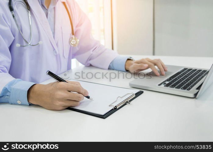 Close up of unknown male doctor sitting at the table near the window in hospital and typing at laptop computer