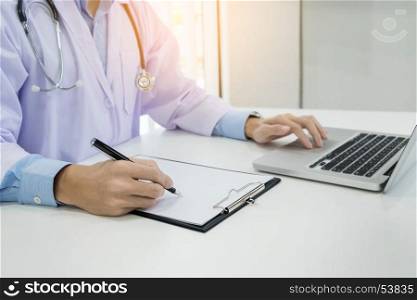 Close up of unknown male doctor sitting at the table near the window in hospital and typing at laptop computer
