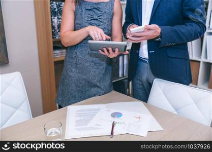 Close up of unrecognizable colleagues looking smartphone and electronic tablet in a business meeting. Unrecognizable colleagues looking electronic devices in meeting