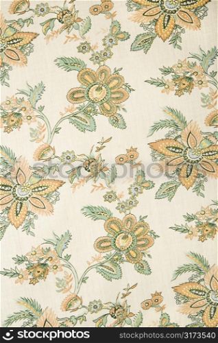 Close-up of vintage fabric with golden flowers and green leaves printed on polyester.